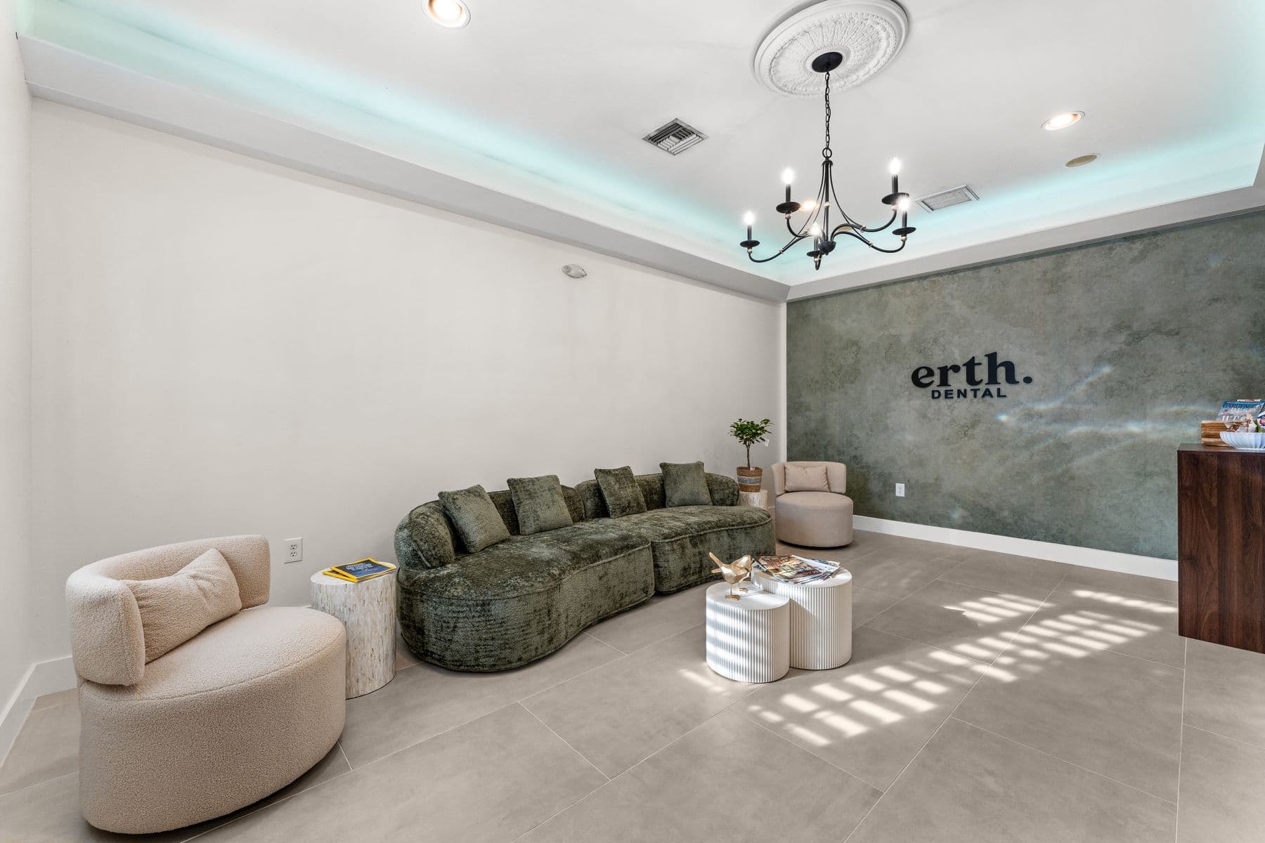 The erth. dental lounge with a green velvet sofa, a chandelier and the practice name on a sage plaster wall