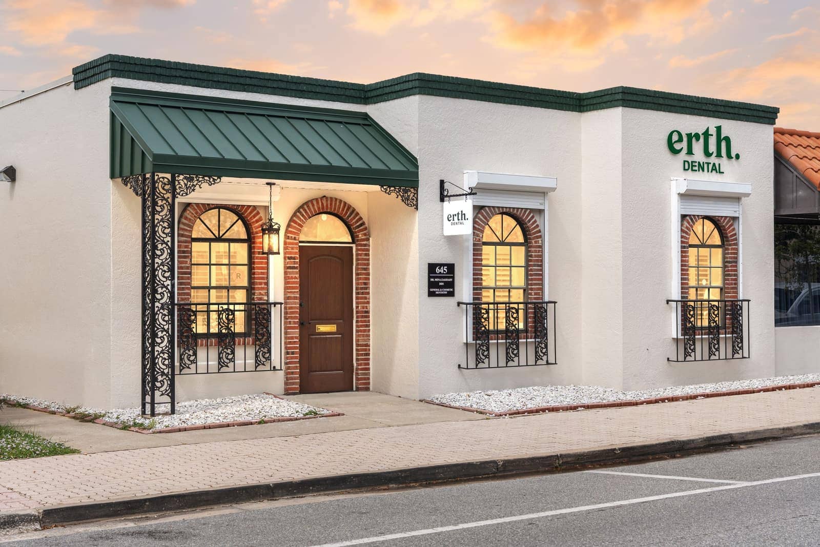 The erth. dental building on Brevard Avenue at dusk, with a green metal awning, brick arches and warmly lit windows