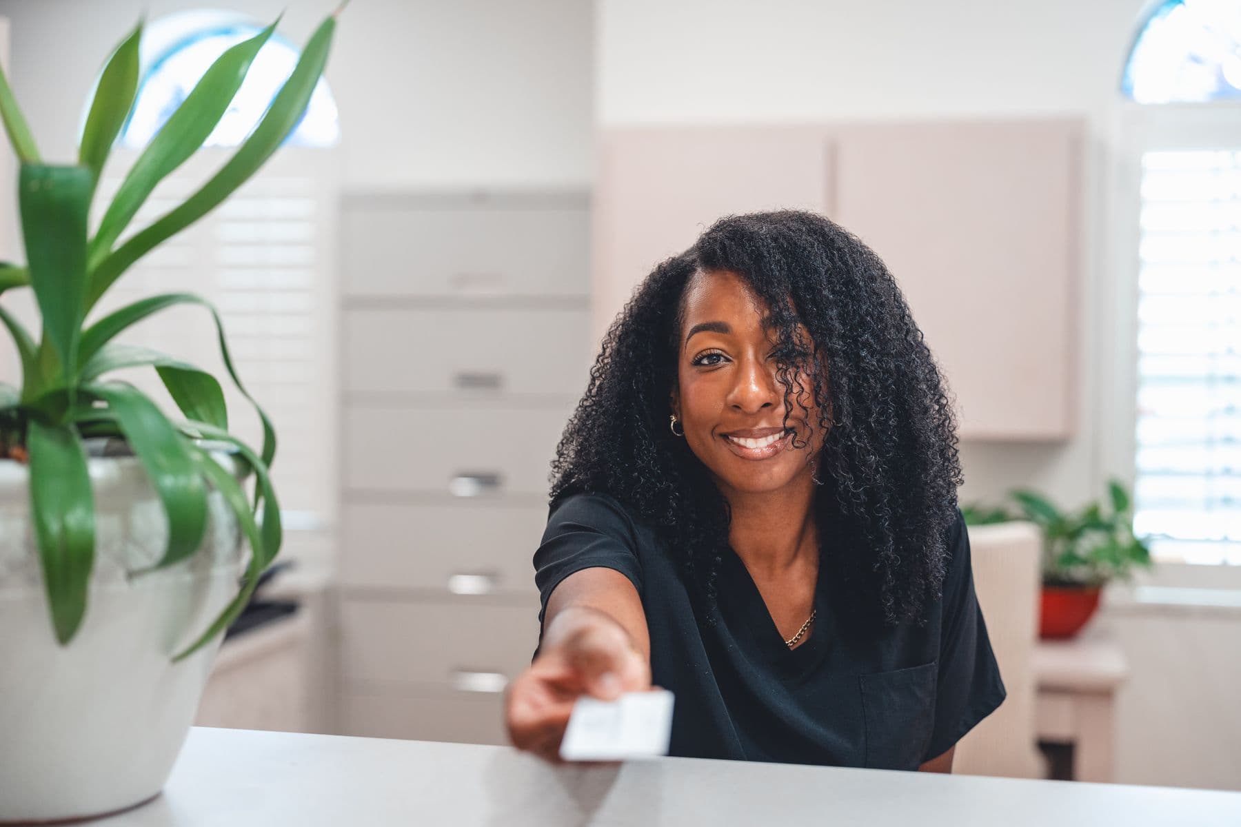 A smiling team member at the erth. dental front desk, handing a card across the counter